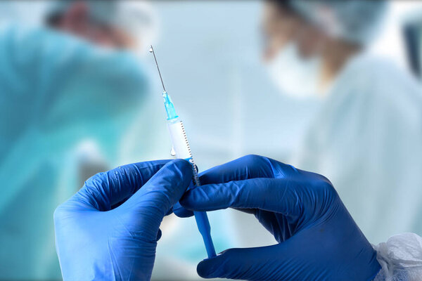 Закройте врачом шприц. Врач в хирургической маске и перчатках готовит шприц для инъекции