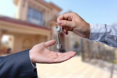 Başka bir ele anahtar veren bir el. Arka plandaki ev.