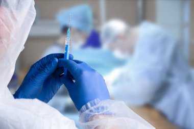 Close up man doctor holding syringe. Doctor in surgical mask and gloves preparing syringe for injection