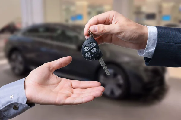 Auto business, car sale, transportation, people and ownership concept - close up of car salesman giving key to new owner or customer over auto show background