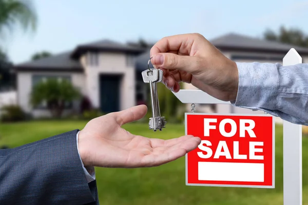 Real Estate Agent Handing Over the House Keys in Front of a Beautiful New Home and For Sale Real Estate Sign