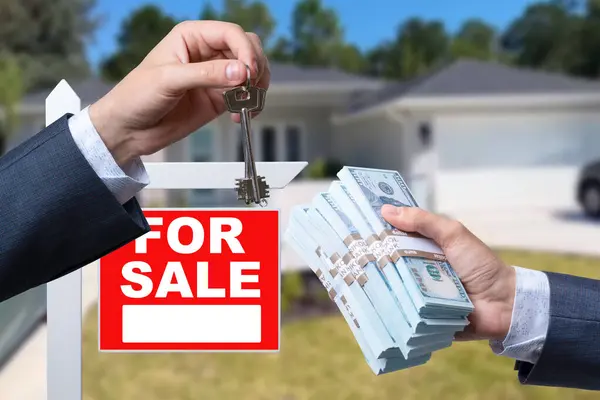 Agent Handing Over Keys as Buyer is Handing Over Cash for House with Home and For Sale Real Estate Sign Behind