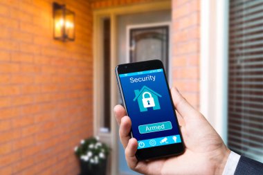 Adam ön kapının arkasındaki cep telefonu uygulamasını kullanarak akıllı ev cihazlarını kontrol ediyor. Dijitalleştirme kavramı. El ele tutuşan bir model.