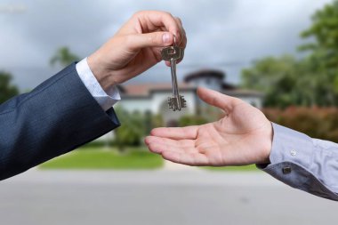 Başka bir ele anahtar veren bir el. Arka plandaki ev.