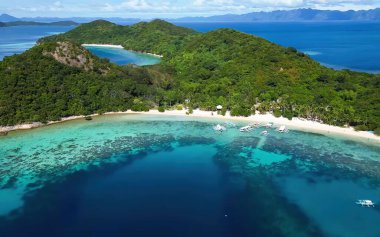 Güneşli bir gökyüzünün altındaki küçük, yemyeşil adaları çevreleyen mavi okyanusun muhteşem hava manzarası..