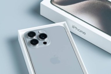 Apple iPhone 15 Pro Max, üç arka kameralı kutusuz akıllı telefon, parlak tasarımını vurgulamak için gri bir yüzeye izole edilmiş..