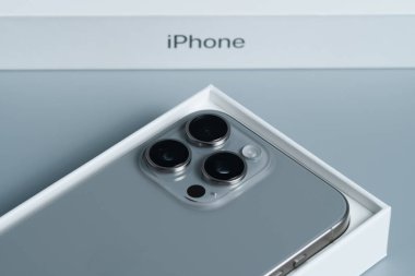 Apple iPhone 15 Pro Max, üçlü lens teknolojisi olan modern bir telefon, boks yaptıktan sonra pürüzsüz gri bir yüzeye izole edilmiş..