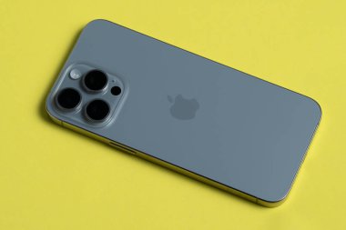 Kutusuz iPhone 15 Pro Max, üç arka lensli, keskin odak detayına sahip sarı bir arka planda izole edilmiş..