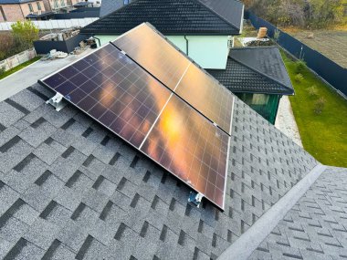 Fotovoltaik panellerle donatılmış modern ev çatısı güneş ışığını yenilenebilir enerjiye dönüştürüyor..