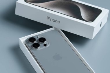 Apple iPhone 15 Pro Max, üç kameralı akıllı telefon yüksek detaylarla çekildi, seçici odaklı gri bir arkaplan üzerine serildi.