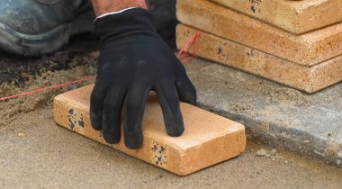 Bir işçi dikkatle bir tuğlayı yeni dökülmüş kumun üzerine yerleştirir. Görev öğleden sonra, inşaat sürecinde doğruluk ve zanaatkarlık üzerine yoğunlaşarak gerçekleşiyor..