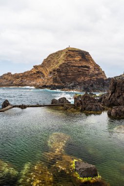 Atlantic Ocean with natural pool and rocky isle with lighthouse near Porto Moniz in Madeira during cloudy springtime day