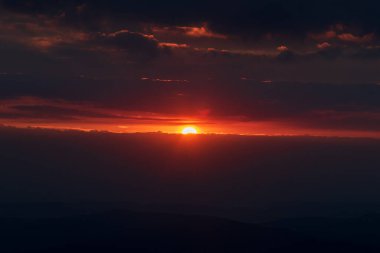 Krkonose dağlarındaki Snezka tepesinden karanlık bulutlar, güneş ve renkli gökyüzü ile gün doğumu