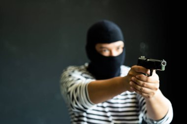 Silahlı maskeli bir soyguncu. Olgun bir adamla silahlı saldırı ve suç kavramı. Siyah üzerine silahlı soygun.. 