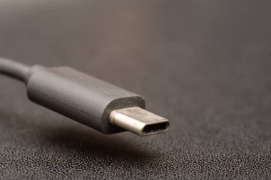 USB tip C bağlantısını koyu arkaplanda gri bir kablo ile kapat. Gri tip c kablosunun kenar yakın plan fotoğrafı.