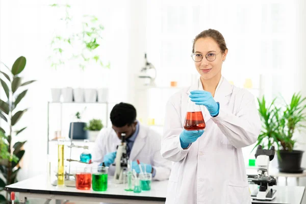 Happy Female scientist working in lab. Smiling Scientist woman with Red liquid in a researcher test tube.