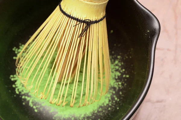 Matcha green tea cooking process in a black bowl with bamboo whisk. Organic green tea matcha powder. Selective focus.