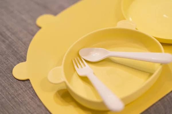 Yellow feeding set. Silicone baby bib, plate, cutlery. Toddler self feeding training, baby weaning concept. Set of plastic dish ware serving baby food.