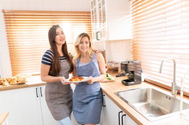 A happy young lesbian couple holding a pizza in the kitchen. The concept of home-cooked food and LGBT relationships. family and diversity concept. lgbt.