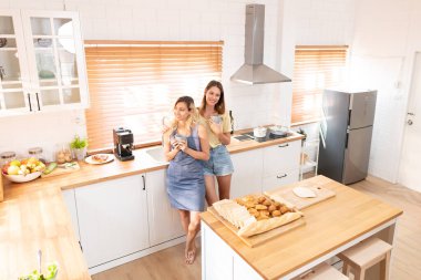 Couple of lesbian Girls Enjoy coffee at home taking about something. Two young adult beautiful women drink tea in modern kitchen 