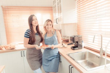 A happy young lesbian couple holding a pizza in the kitchen. The concept of home-cooked food and LGBT relationships. family and diversity concept. lgbt. warm tone.