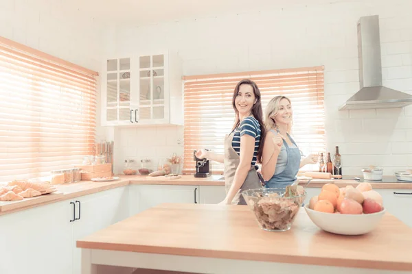 Happy LGBT lesbian couple dancing while cooking together at home. Girl dancing and turning, enjoying togetherness at background neon sign with word Together. Concept lgbt couple. warm tone.