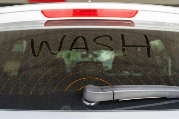 Dirty rear window of the car and inscription Wash. Wash Text on Dirty Car.