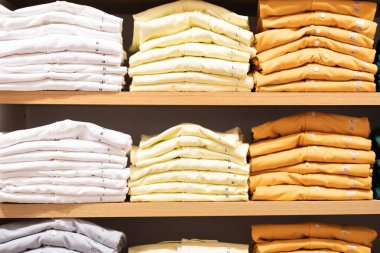 Kumaş dükkanındaki masanın üstünde bir yığın renkli kıyafet var.. 