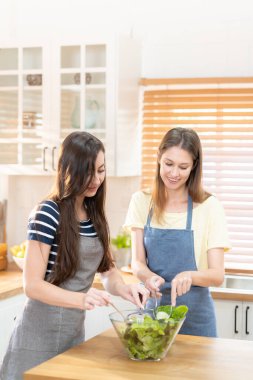 Mutfakta salata pişiren mutlu ve gülümseyen lezbiyen çift. Birlikte yemek pişirirken tatlı gülüşlü cam kasede salata. Eşcinsel eşitlik ve farklılıkları desteklemek için gurur ayı.