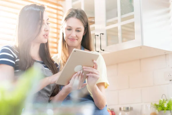 stock image Beautiful lesbian couple cooking healthy food, looking on digital tablet at modern kitchen interior. Homosexual relations and healthy eating concept.  LGBTQ+,LGBT,LGBTQ home online kitchen.