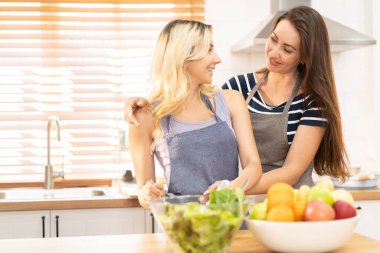 Mutfakta salata pişiren mutlu ve gülümseyen lezbiyen çift. Birlikte yemek pişirirken tatlı gülüşlü cam kasede salata. Eşcinsel eşitlik ve farklılıkları desteklemek için gurur ayı.