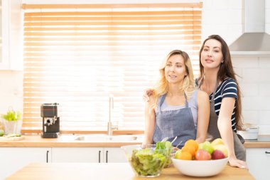 Happy LGBT lesbian couple dancing while cooking together at home. Girl dancing and turning, enjoying togetherness at background neon sign with word Together. Concept lgbt couple.