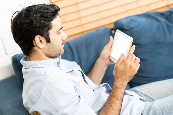 stock image Handsome man is using a digital tablet while resting on couch at home. man sitting on sofa and holding tablet computer with isolated screen