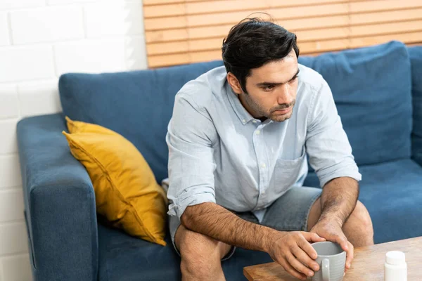 Unhappy man thinking about health or something bad on his sofa at home in the living room. upset man having problems, side view, copy space. Loneliness, depression, financial hangover concept.