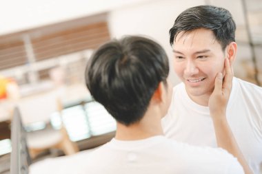 Mutlu Asyalı eşcinsel çift kanepede birbirine sarılıyor. Asyalı LGBT çifti evde kucaklaşıyor. LGBT ilişkilerinin çeşitliliği. Eşcinsel çift kavramı. LGBT çoklu ilişkisi.