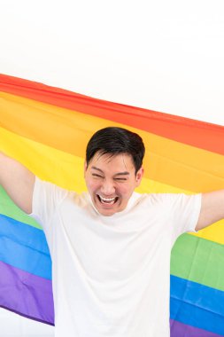 Gökkuşağı bayrağına sarılı neşeli genç adam beyaz arka planda izole edilmiş eğleniyor. Homoseksüel Igbtiq konsepti, gökkuşağı bayrağı, kutlama geçidi. Boşluğu kopyala.