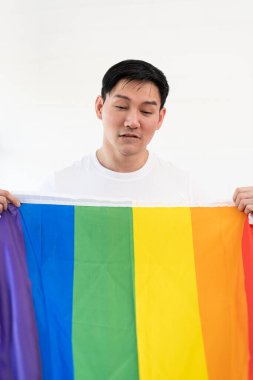 Gökkuşağı bayrağına sarılı neşeli genç adam beyaz arka planda izole edilmiş eğleniyor. Homoseksüel Igbtiq konsepti, gökkuşağı bayrağı, kutlama geçidi. Boşluğu kopyala.