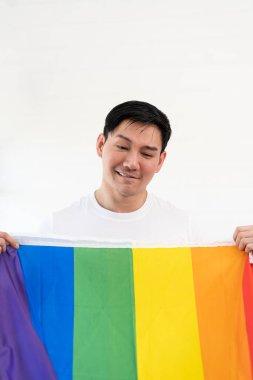 Gökkuşağı bayrağına sarılı neşeli genç adam beyaz arka planda izole edilmiş eğleniyor. Homoseksüel Igbtiq konsepti, gökkuşağı bayrağı, kutlama geçidi. Boşluğu kopyala.