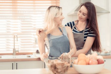Mutfakta salata pişiren mutlu ve gülümseyen lezbiyen çift. Birlikte yemek pişirirken tatlı gülüşlü cam kasede salata. Eşcinsel eşitlik ve farklılıkları teşvik etmek için gurur ayı. sıcak ton.