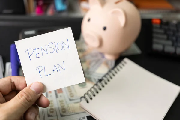 Paper note with text PENSION PLAN with stationery on desk. Pension Plan. Retirement concept. Pension calculation concept. copy space for text. Piggy bank.