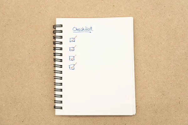 Top view of notebook with handwritten Checklist text. Checklist concept, checklist box with red checkmark.