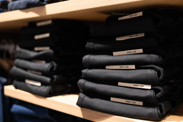 Stacks of folded jeans on the shop shelves in the showroom or store. Clothes storage. Fashion retail shop inside shopping mall.