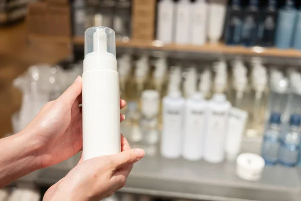 Plastic spray bottle with pump in hand at cosmetic store. Dermatologist hands holding blank cosmetic skincare bottle. Foam dispenser for face care. Container with body lotion.