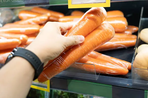 Man\'s hand picked a carrot to look at in grocery department store, Shopping in supermarket. Buying carrots in a supermarket.