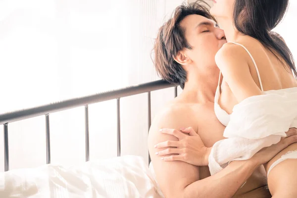 Asian Woman sit on man and embrace him. They look at each other. Sexy passionate young couple hugging on the bed before having sex in the bedroom. Valentine\'s day.