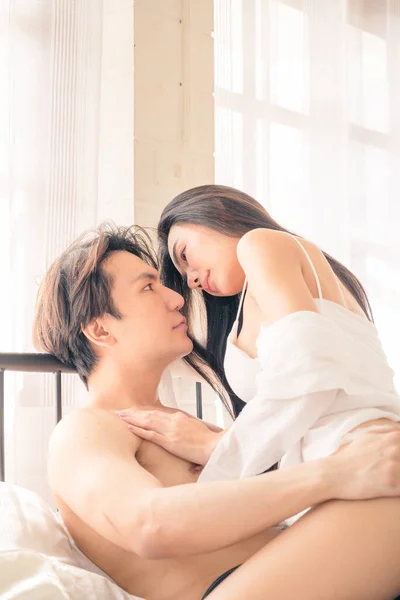 Asian Woman sit on man and embrace him. They look at each other. Sexy passionate young couple hugging on the bed before having sex in the bedroom. Valentine\'s day.