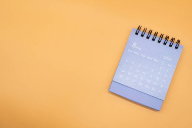 Turuncu arka planda izole edilmiş 2024 AĞUSTOS için mavi masa takvimi. Takvim konsepti kopyalama alanı. Düz yatıyordu.