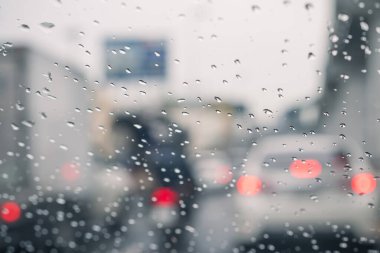 Arabanın camına ve ışıklarına yağmur damlaları düşer. Yağmurlu bir günde arabanın camından geçen trafik ve elektrik ışıklarıyla yapılmış bokeh resmi.