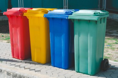 Yerde yeşil, mavi, kırmızı ve sarı çöp kutuları olan atık geri dönüşüm yönetimi kavramı.