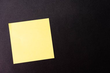 Koyu arkaplanda boş sarı yapışkan bir not var. Boşluğu kopyala.